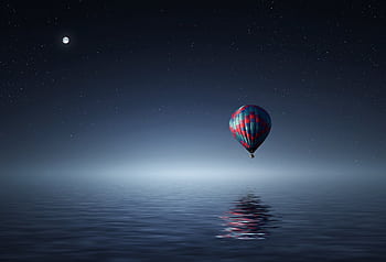 A serene hot air balloon floating over the ocean under a starry night sky. HD wallpaper