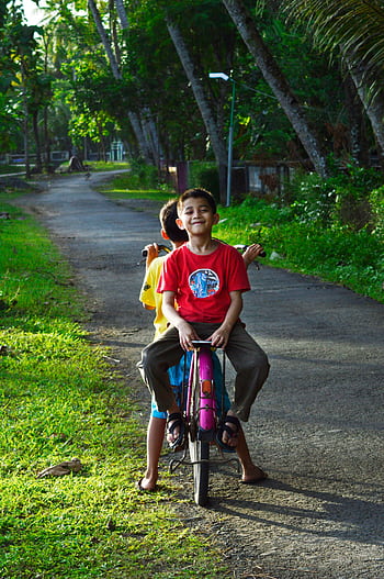 Two children enjoying a bicycle ride in lush Central Java countryside. HD phone wallpaper