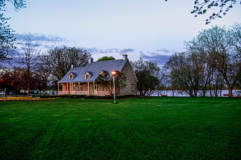 Serene stone house by a lakeside with lush green lawn, ideal for real estate and architectural themes. HD wallpaper