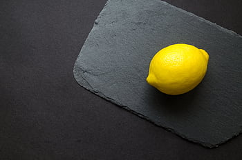 A single fresh lemon placed on a dark slate, highlighting its vibrant yellow color. HD wallpaper