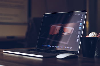 A sleek laptop on a wooden desk with a cup, creating a warm and cozy workspace atmosphere. HD wallpaper