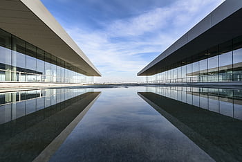 Futuristic glass building mirrored on a still water surface with a cloudy sky. HD wallpaper