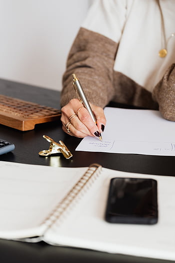 A businesswoman writing notes with a pen at a modern office desk. HD phone wallpaper
