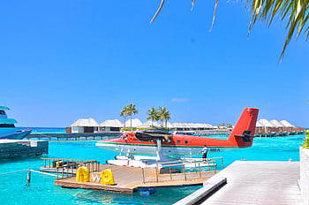 Seaplane docked at a vibrant tropical island resort under a clear blue sky, perfect for vacations. HD wallpaper