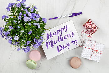 Flat lay of Mother's Day card with purple flowers, gift, macarons, and a pen indoors. HD wallpaper