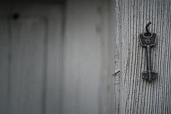 A vintage iron key hangs on a textured weathered wooden wall, evoking nostalgia and mystery. HD wallpaper