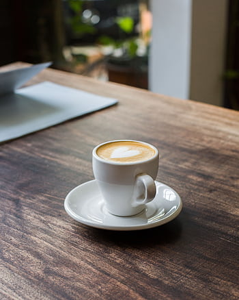 A serene moment with a cappuccino on a wooden table, featuring latte art in a cozy café setting. HD phone wallpaper