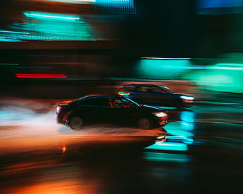 Long exposure shot capturing the vibrant motion blur of cars speeding through a city street at night. HD wallpaper