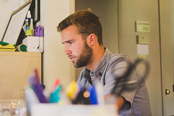 A young man with a beard intensely working at a desk in an office environment. HD wallpaper