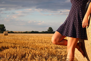 A woman in a polka dot dress leans against a hay bale in a sunlit wheat field. HD wallpaper