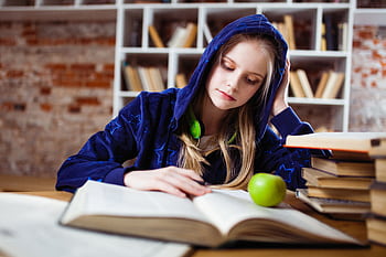 Teenage girl in blue hood reads in library, heads and apple by her side. HD wallpaper