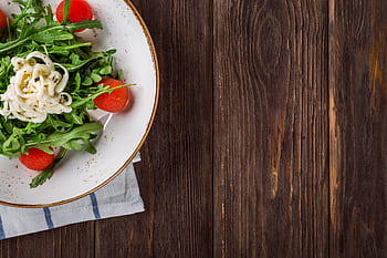 A delightful arugula salad with tomatoes and cheese, served on a rustic wooden table, perfect for healthy eating. HD wallpaper