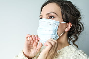 Adult woman adjusting blue surgical mask indoors for health safety. HD wallpaper