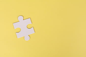 Simple white jigsaw puzzle piece placed on a bright yellow background with ample copy space. HD wallpaper