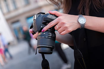 A woman adjusting a DSLR camera outdoors, focusing on her hands and device. Perfect for graphy themes. HD wallpaper