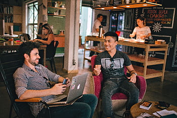Two men enjoying a relaxed conversation with laptops in a cozy Brazilian café. HD wallpaper