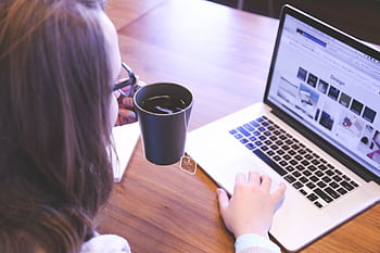 A woman enjoys coffee while browsing the web on a laptop at a home office desk. HD wallpaper