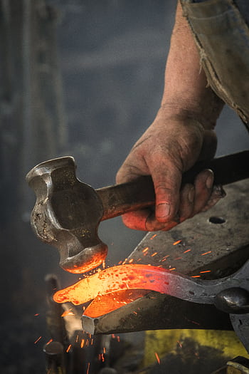 Close-up of a blacksmith hammering a hot iron piece in a workshop. HD phone wallpaper