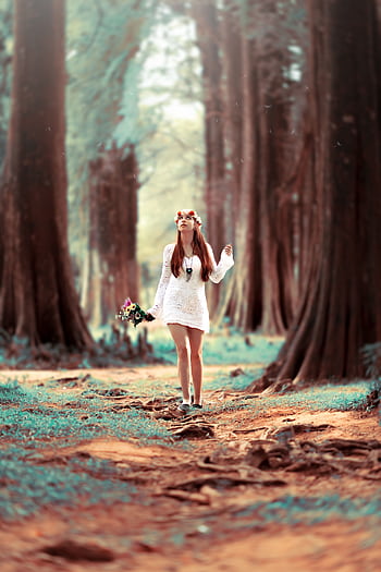 A young woman in a white dress enjoys a leisure walk in a serene forest setting. HD phone wallpaper
