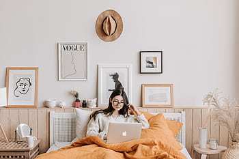 Young woman in cozy bedroom using a laptop, surrounded by stylish decor and art. HD wallpaper