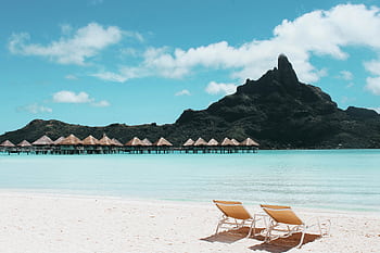 Pristine beach with loungers facing turquoise waters and iconic Mount Otemanu in French Polynesia. HD wallpaper