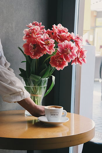 A serene indoor scene with fresh pink tulips in a vase beside a coffee cup on a wooden table. HD phone wallpaper