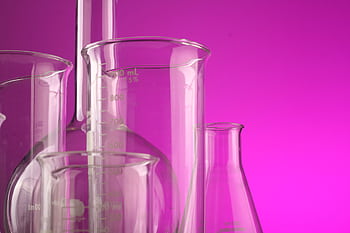Clear glass laboratory flasks with volume measurements against a vibrant purple backdrop, ideal for science themes. HD wallpaper