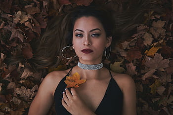 A woman in elegant fashion lies on autumn leaves, showcasing jewelry and style. HD wallpaper