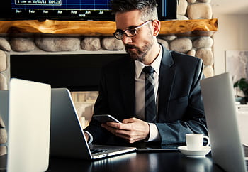 Businessman in formal attire working on a laptop and smart at an indoor office desk. HD wallpaper