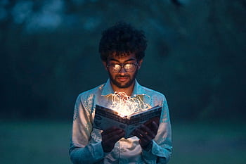 A man with glasses reads an illuminated book outdoors during twilight. HD wallpaper
