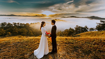 A bride and groom embrace amidst a sea of clouds at sunset in Đà Lạt, creating a romantic scene. HD wallpaper
