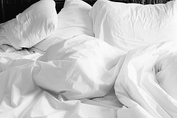 A cozy, rumpled white bed with soft sheets and pillows in a modern bedroom setting. HD wallpaper