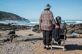 Two senior women enjoying a peaceful moment by the rocky beach, embracing friendship and serenity. HD wallpaper