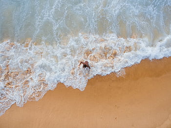 A high-angle aerial shot of a person at the beach with waves crashing on the sand. HD wallpaper