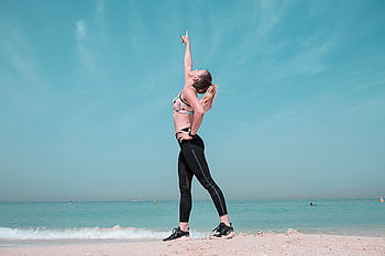 A woman performing a stretching exercise on a sunny beach in Dubai. HD wallpaper