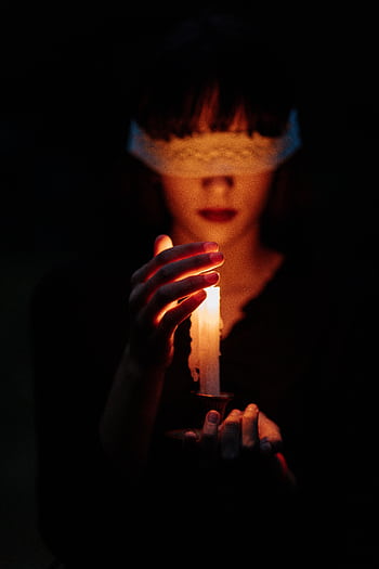 A blindfolded woman holding a lit candle in a dark setting, invoking mystery. HD phone wallpaper