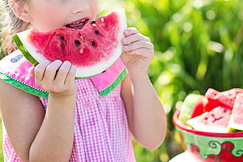 Young girl eating a juicy watermelon slice in a sunny outdoor setting, symbolizing summer refreshment. HD wallpaper
