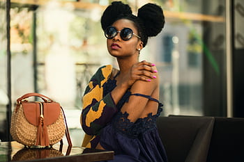 Fashionable woman in a chic outfit and sunglasses sitting indoors with a stylish handbag. HD wallpaper