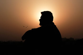 A silhouette of a man sitting in profile against a stunning golden sunset, creating a peaceful and reflective scene. HD wallpaper