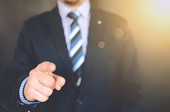 Confident businessman in a suit pointing forward, signifying leadership and focus. HD wallpaper