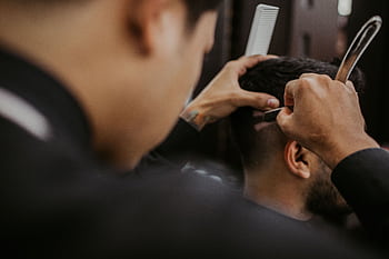 Close-up of a barber expertly styling a man's hair with a razor and comb in a trendy barbershop. HD wallpaper