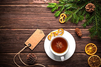 A cozy rustic setting with a teacup, cinnamon, pretzels, and pine decorations on a wooden table. HD wallpaper
