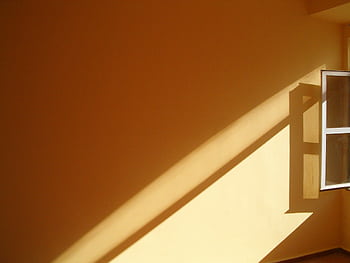 Warm sunlight streams through an open window, creating bold shadows on a yellow wall, offering a minimalist composition. HD wallpaper
