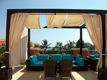 Elegant outdoor seating area on a sunlit rooftop overlooking the ocean. HD wallpaper