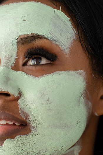 A close-up portrait of a woman with a green clay facial mask focusing on eye detail. HD phone wallpaper