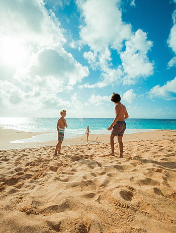 Three children enjoy a sunny day playing on Waialua Beach, Hawaii, with clear skies and blue ocean waters. HD phone wallpaper