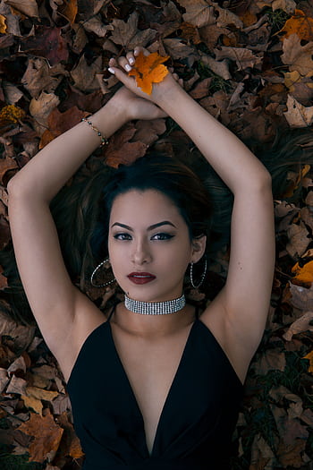 Stylish woman with jewelry in a black dress posing on fall leaves, exuding glamour and elegance. HD phone wallpaper