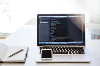 Open laptop displaying code on a desk with smart and notebook, ideal for technology and business use. HD wallpaper