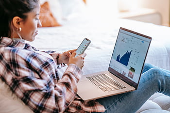 A woman using her and laptop to monitor stock market trends at home. HD wallpaper