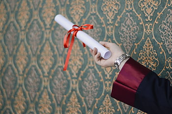 A graduate's hand holding a diploma with red ribbon, symbolizing achievement. HD wallpaper